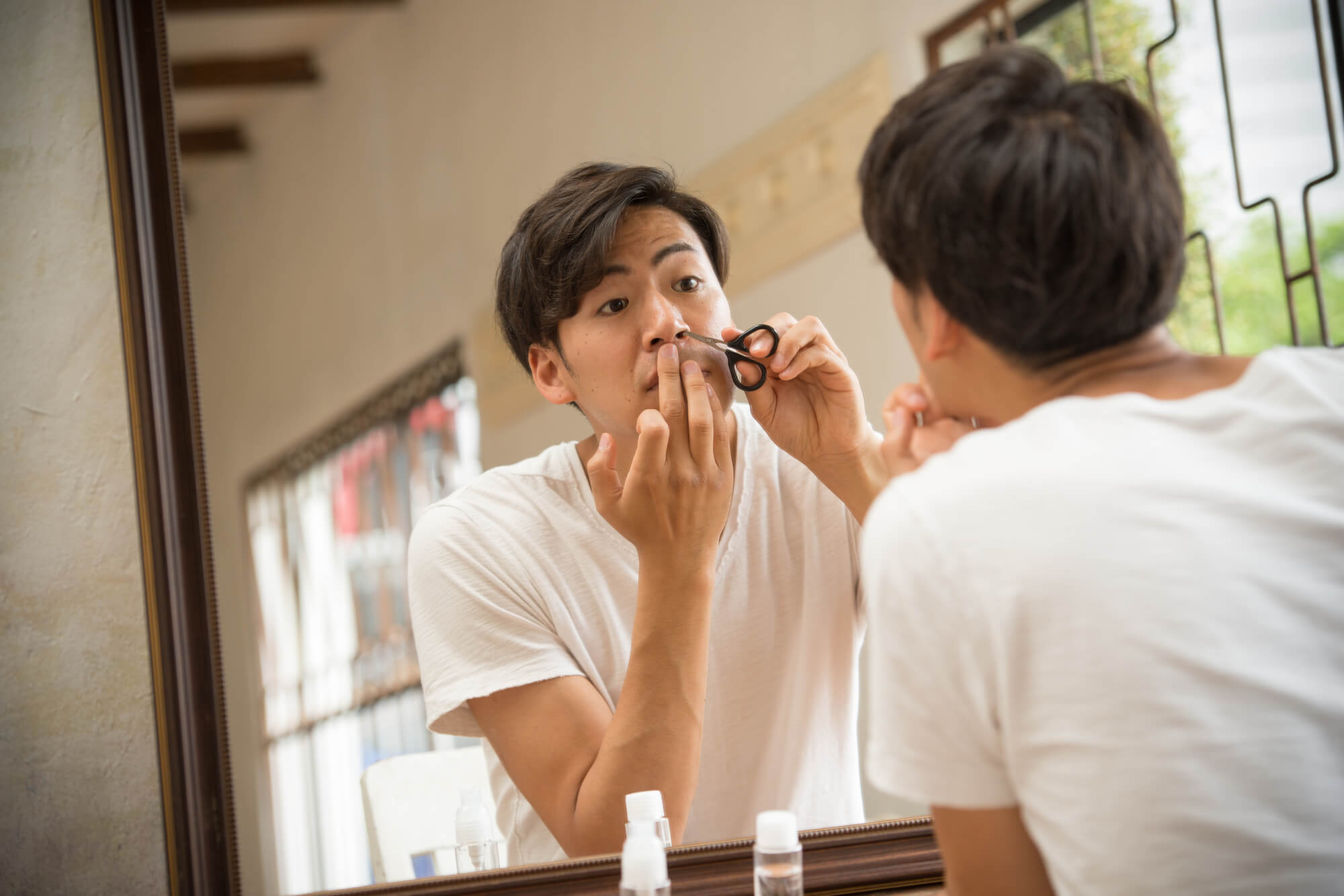 鏡を見て鼻まわりの身だしなみを整える男性